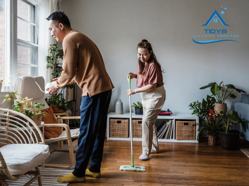 Couple cleaning a bright living room while watering green houseplants